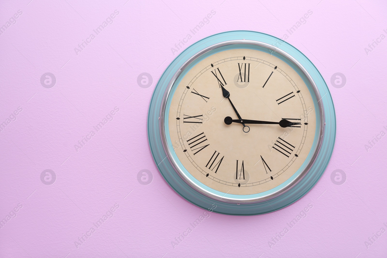 Photo of Stylish clock with Roman numerals on color wall. Time of day