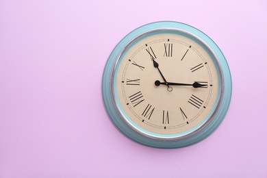 Photo of Stylish clock with Roman numerals on color wall. Time of day
