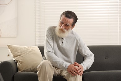 Senior man suffering from knee pain on sofa at home. Rheumatism symptom