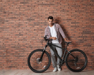 Photo of Handsome young man with modern bicycle near brick wall indoors