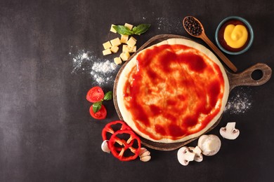 Photo of Pizza dough smeared with tomato sauce and products on dark table, flat lay. Space for text