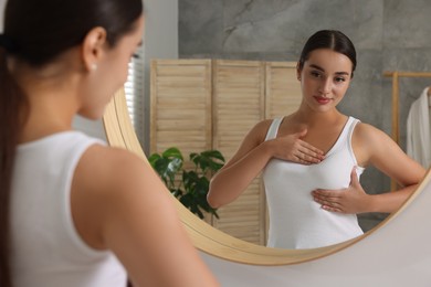 Photo of Beautiful young woman doing breast self-examination near mirror in bathroom