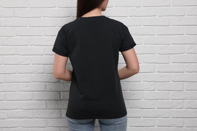 Woman wearing stylish black T-shirt near white brick wall, closeup