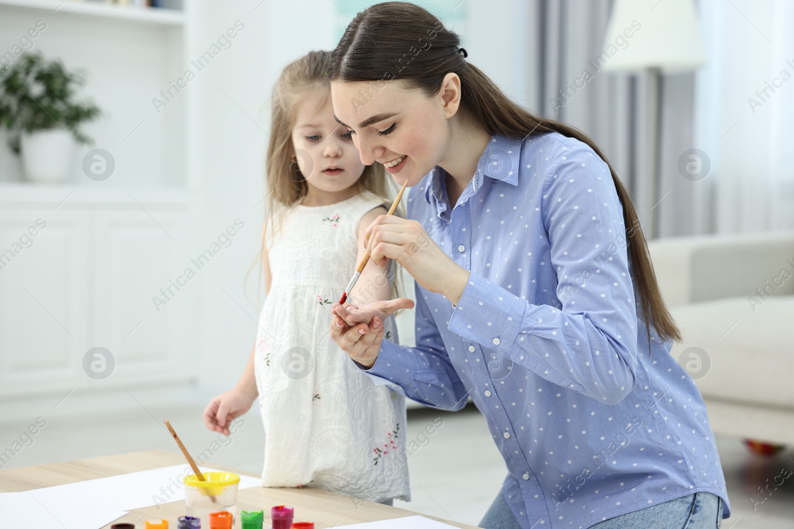 Photo of Mother and her little daughter painting with palms at home