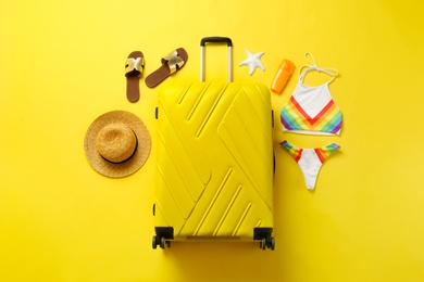 Photo of Flat lay composition with suitcase, bikini and beach accessories on color background