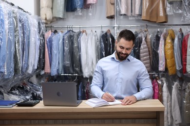 Dry-cleaning service. Happy worker taking notes at counter indoors