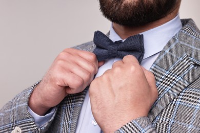 Photo of Man adjusting bow tie on grey background, closeup