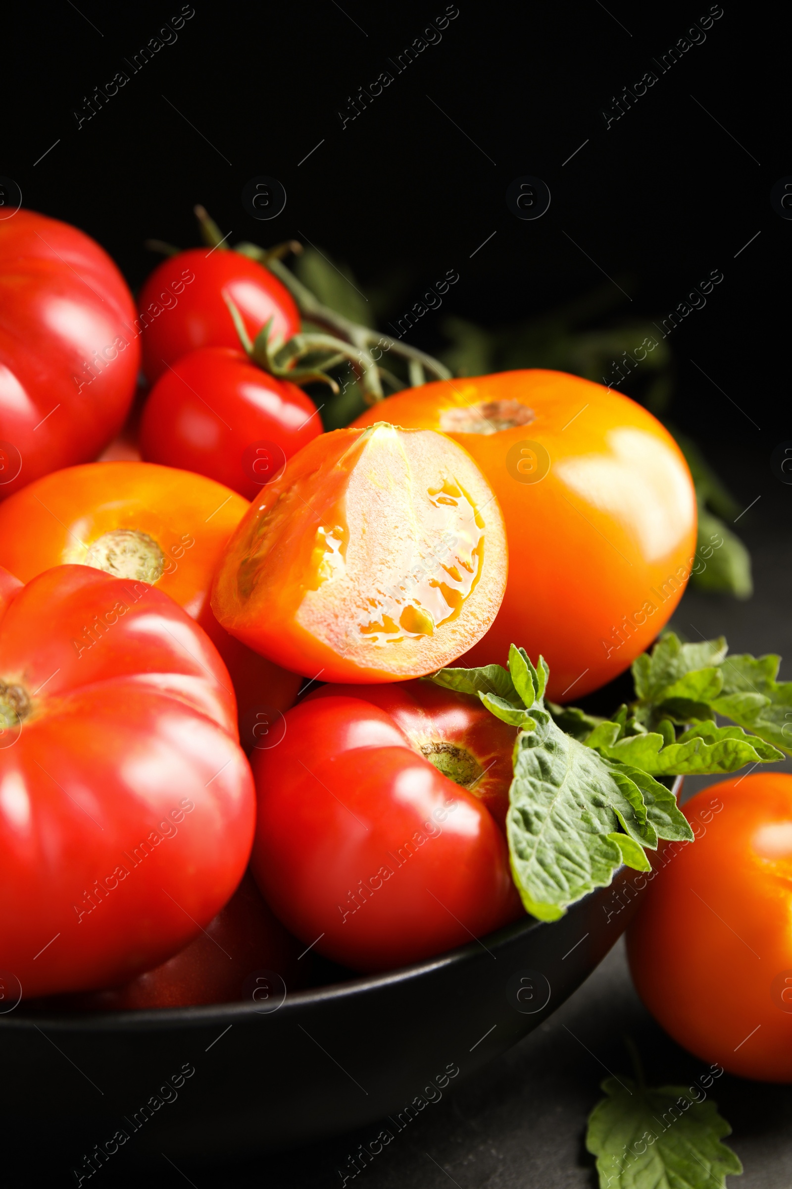 Photo of Many different ripe tomatoes with leaves on black table, closeup