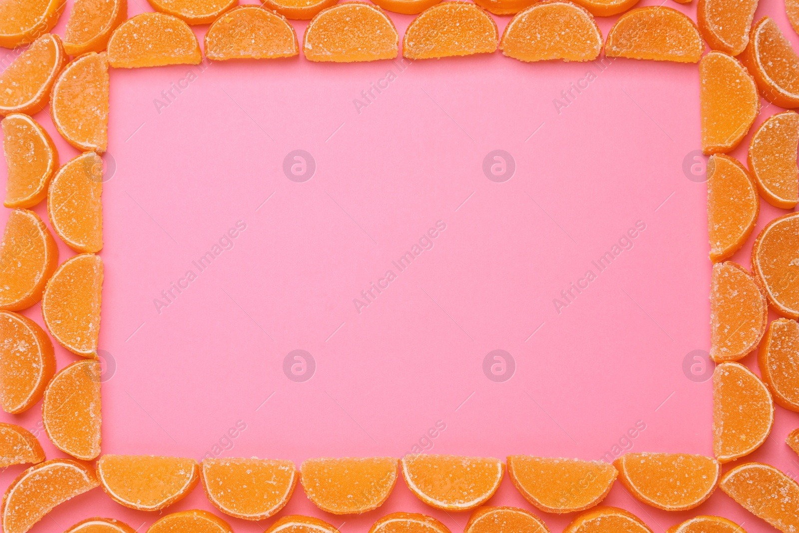 Photo of Frame made with orange marmalade candies on pink background, flat lay