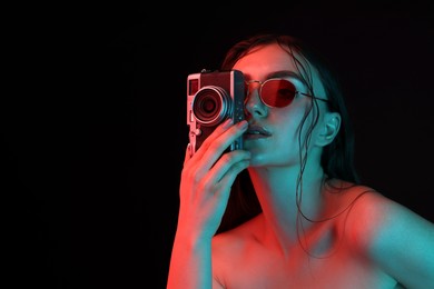 Photo of Beautiful woman with sunglasses and vintage camera posing in neon lights against black background. Space for text