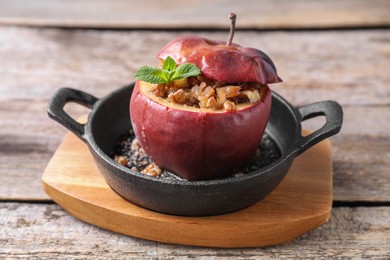 Photo of Tasty baked apple with nuts, honey and mint in baking dish on wooden table