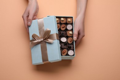 Photo of Woman with open box of delicious chocolate candies on beige background, top view