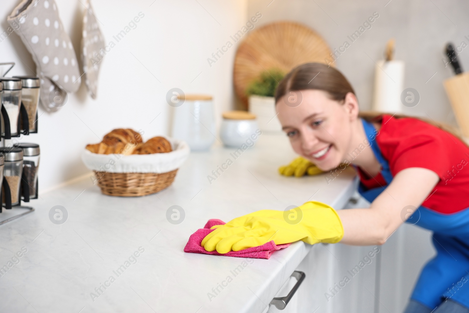 Photo of Woman cleaning white countertop with rag in kitchen, selective focus