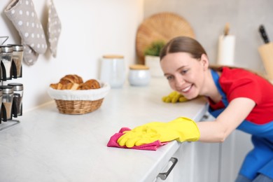 Photo of Woman cleaning white countertop with rag in kitchen, selective focus