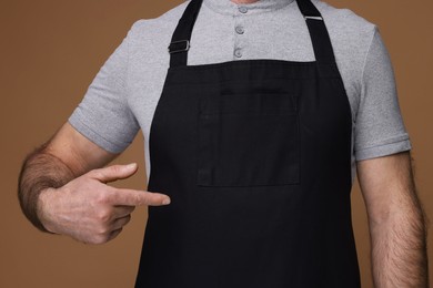 Photo of Man pointing at kitchen apron on brown background, closeup. Mockup for design