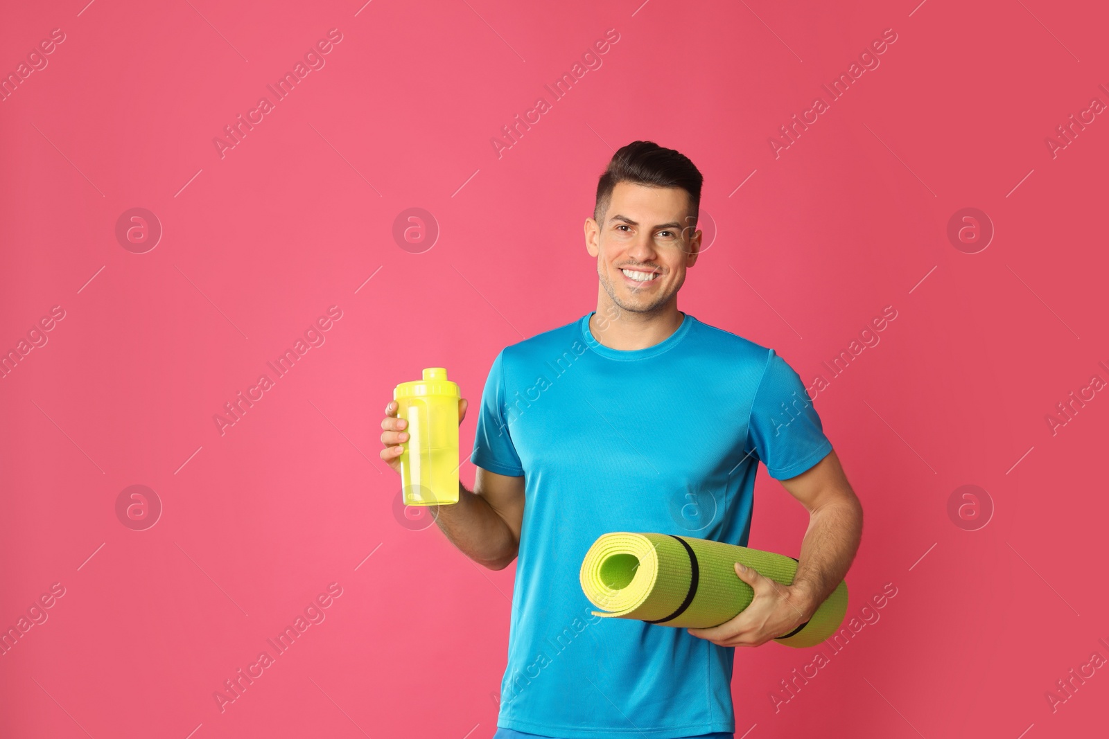 Photo of Handsome man with yoga mat and shaker on pink background