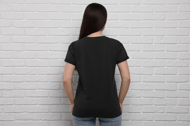 Photo of Woman wearing stylish black T-shirt near white brick wall, back view