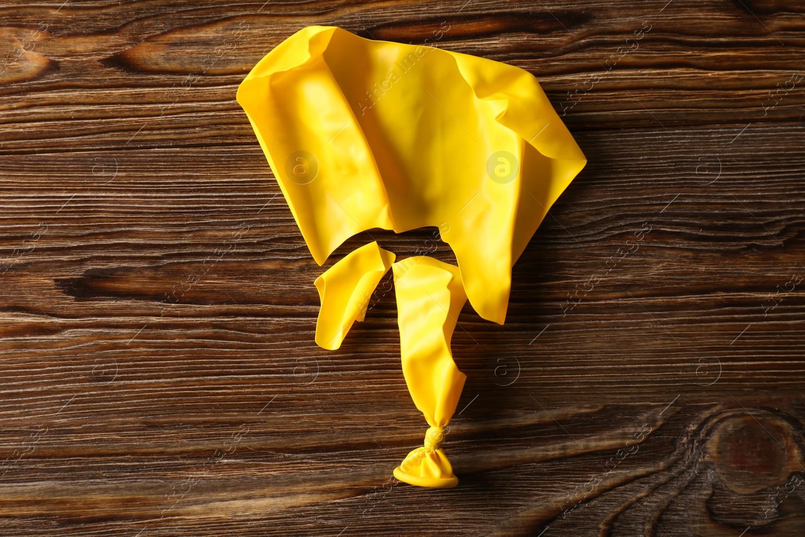 Photo of Popped yellow balloon on wooden background, top view