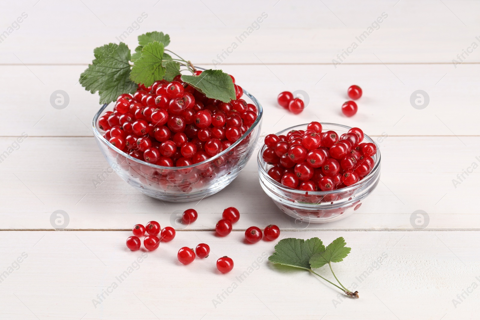 Photo of Many ripe red currants and leaves on white wooden table