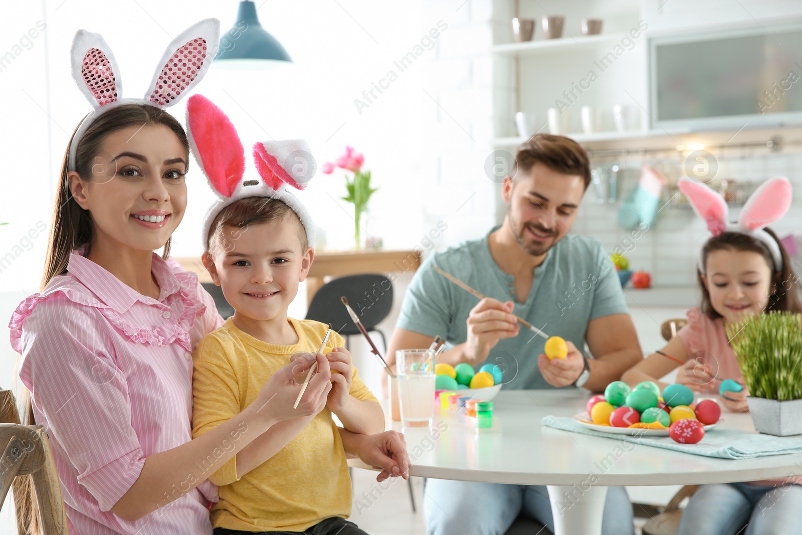 Photo of Happy family painting Easter eggs in kitchen. Festive tradition