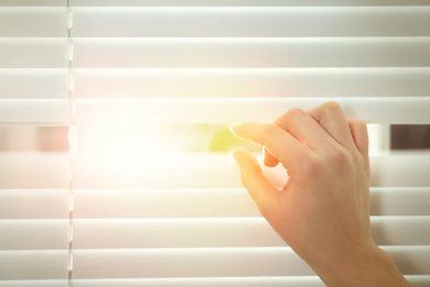 Image of Woman opening window blinds on sunny morning, closeup