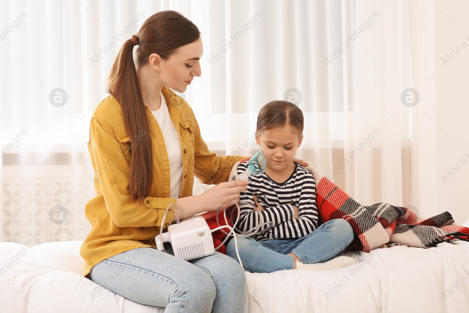 Photo of Mother helping her sick daughter with nebulizer inhalation in bedroom