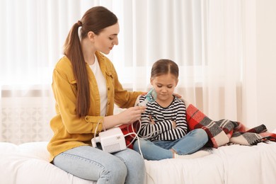 Mother helping her sick daughter with nebulizer inhalation in bedroom