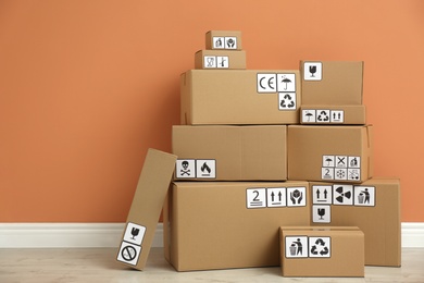 Photo of Cardboard boxes with different packaging symbols on floor near orange wall. Parcel delivery