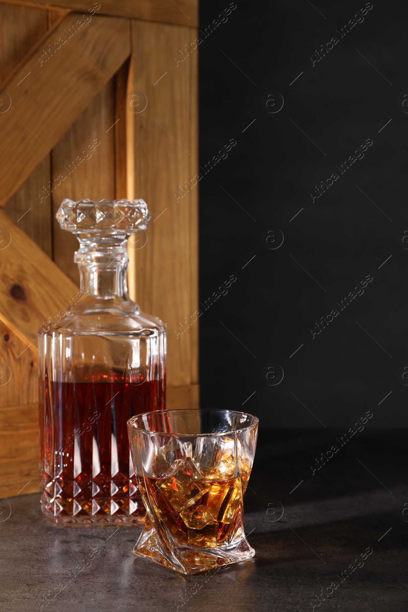 Photo of Whiskey with ice cubes in glass and bottle on grey table