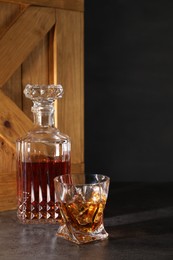 Whiskey with ice cubes in glass and bottle on grey table