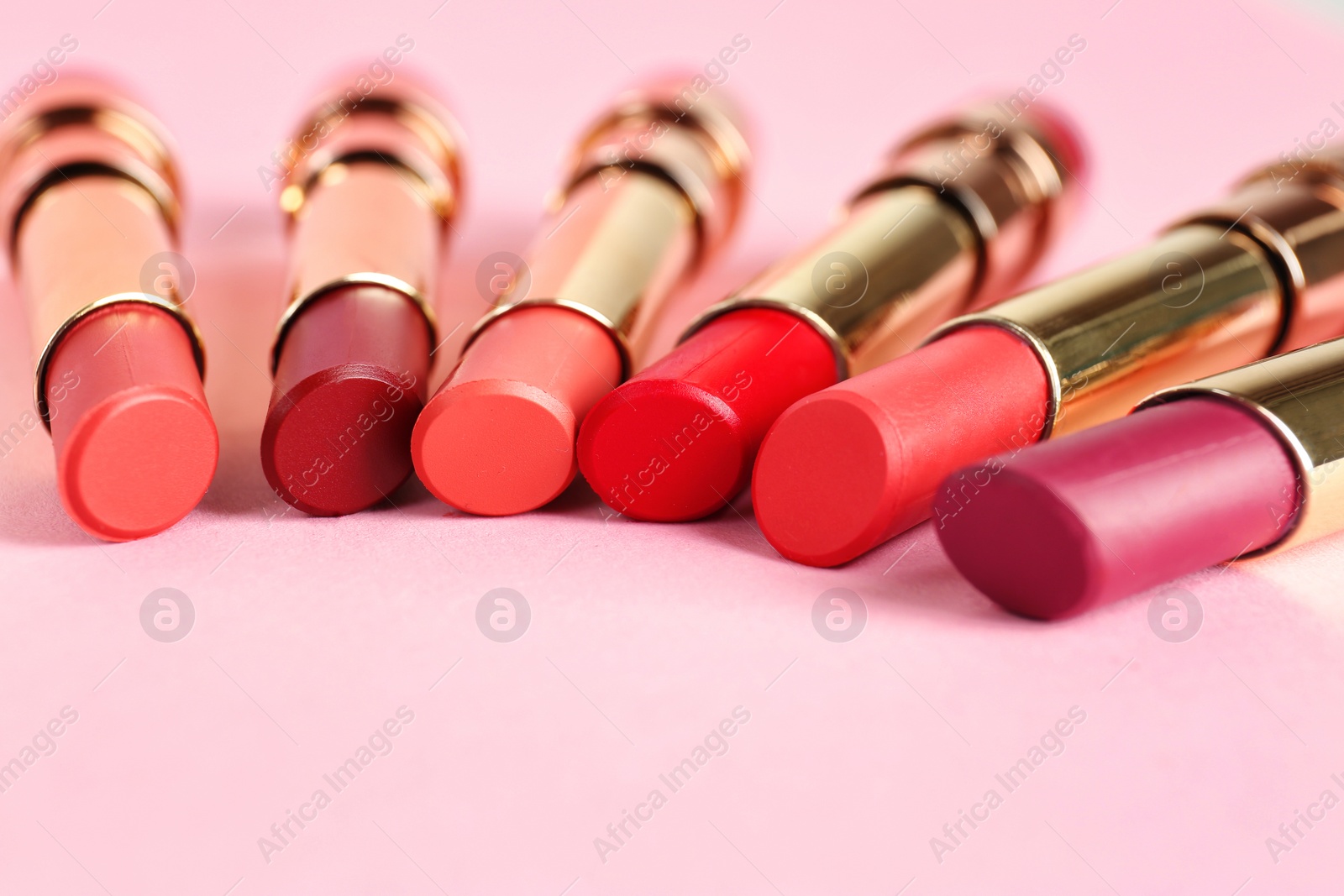 Photo of Set of bright lipsticks in gold tubes on pink background, space for text