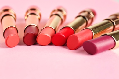 Photo of Set of bright lipsticks in gold tubes on pink background, space for text