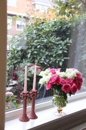 Photo of Vase with beautiful bouquet of roses and candles on windowsill indoors