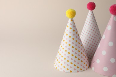 Photo of Beautiful party hats with pompoms on beige background. Space for text