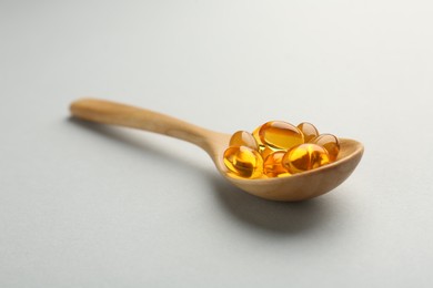 Photo of Vitamin capsules in wooden spoon on light grey background, closeup. Health supplement