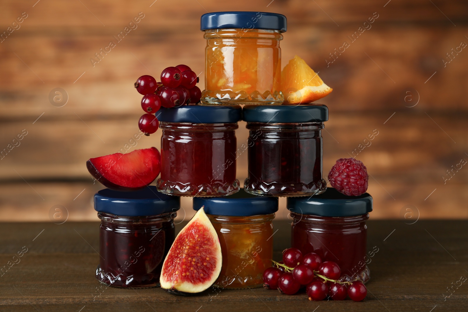 Photo of Jars of different jams and fresh ingredients on wooden table