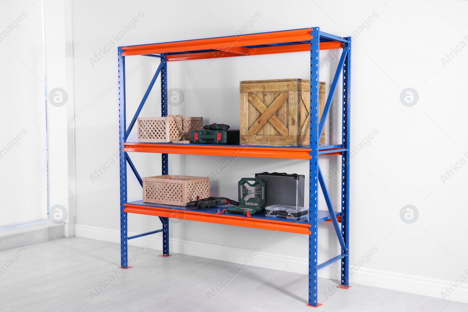 Photo of Metal shelving unit with wooden crates and different instruments near light wall indoors