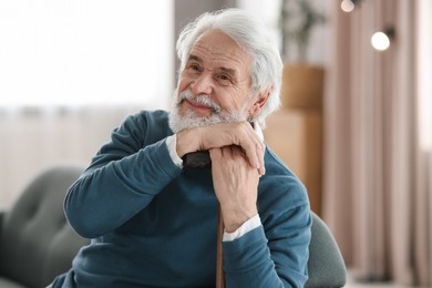 Photo of Portrait of happy grandpa with walking cane sitting on sofa indoors