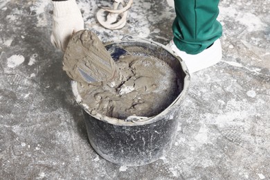 Worker with trowel mixing concrete in bucket indoors, closeup