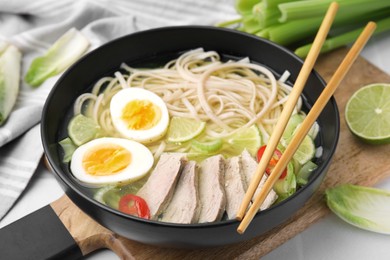 Photo of Bowl of delicious rice noodle soup with meat and egg on white table, closeup