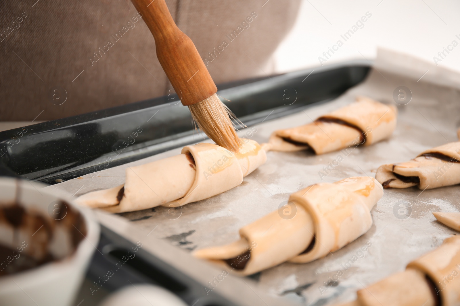 Photo of Woman spreading egg yolk on croissants, closeup