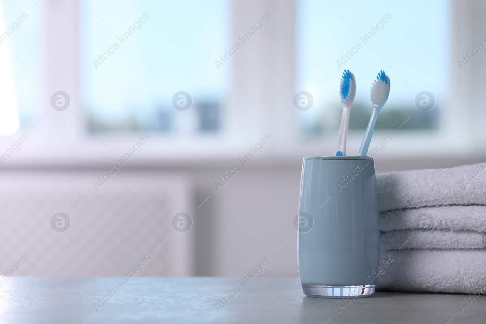 Photo of Plastic toothbrushes in holder and towels on light grey table indoors. Space for text