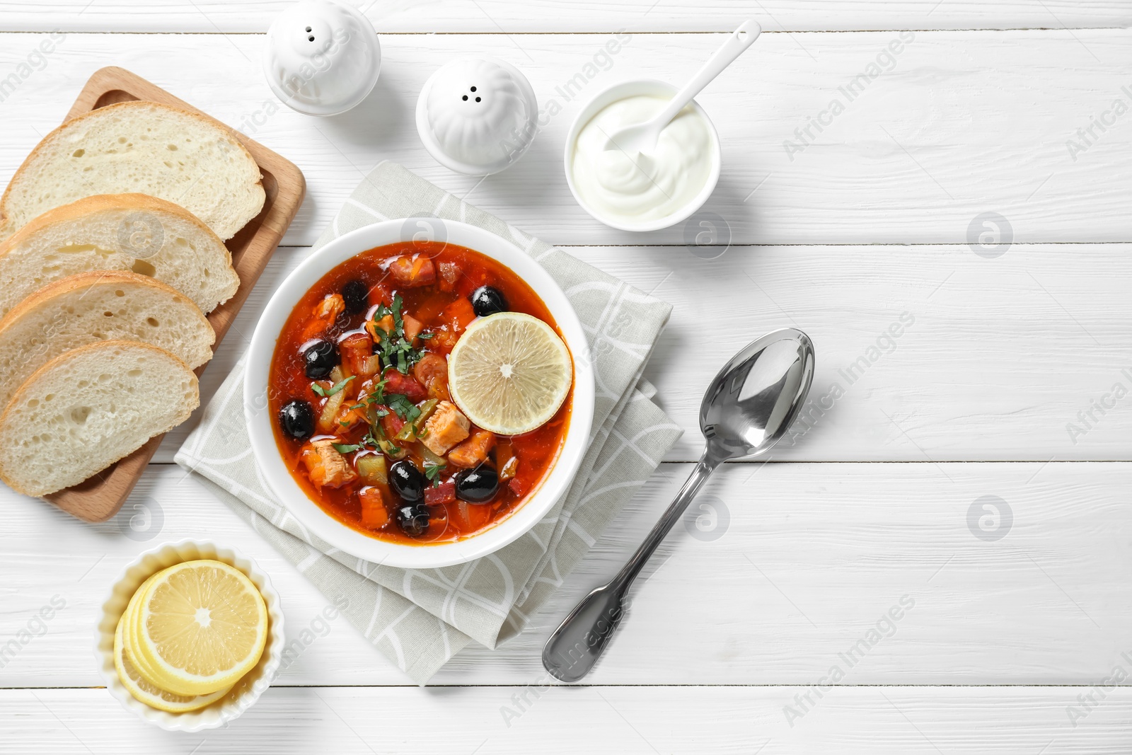 Photo of Meat solyanka soup with sausages, olives and vegetables served on white wooden table, flat lay. Space for text