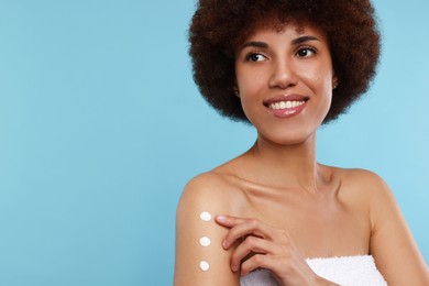 Photo of Beautiful young woman applying body cream onto arm on light blue background, space for text