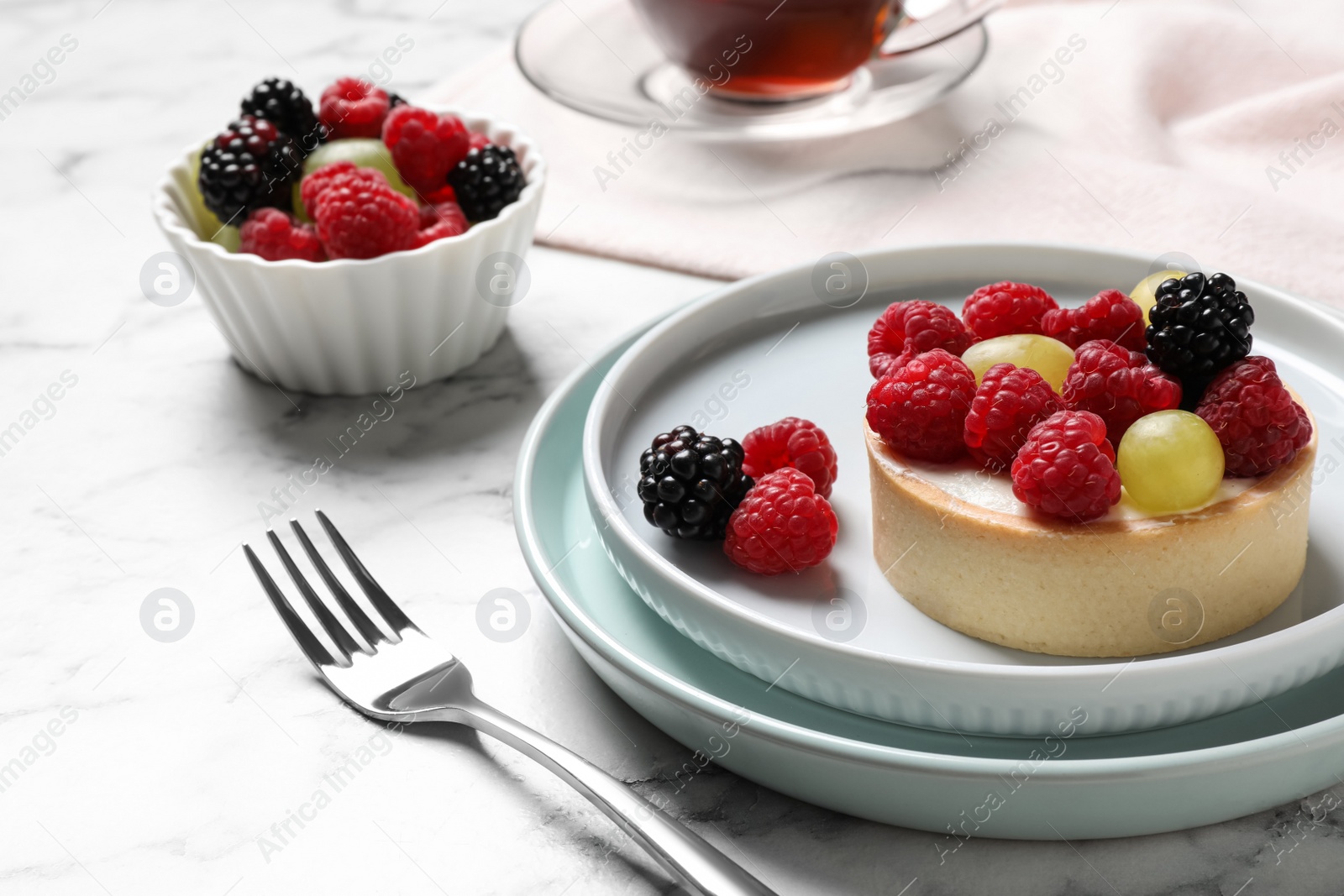 Photo of Delicious tartlet with berries on white marble table