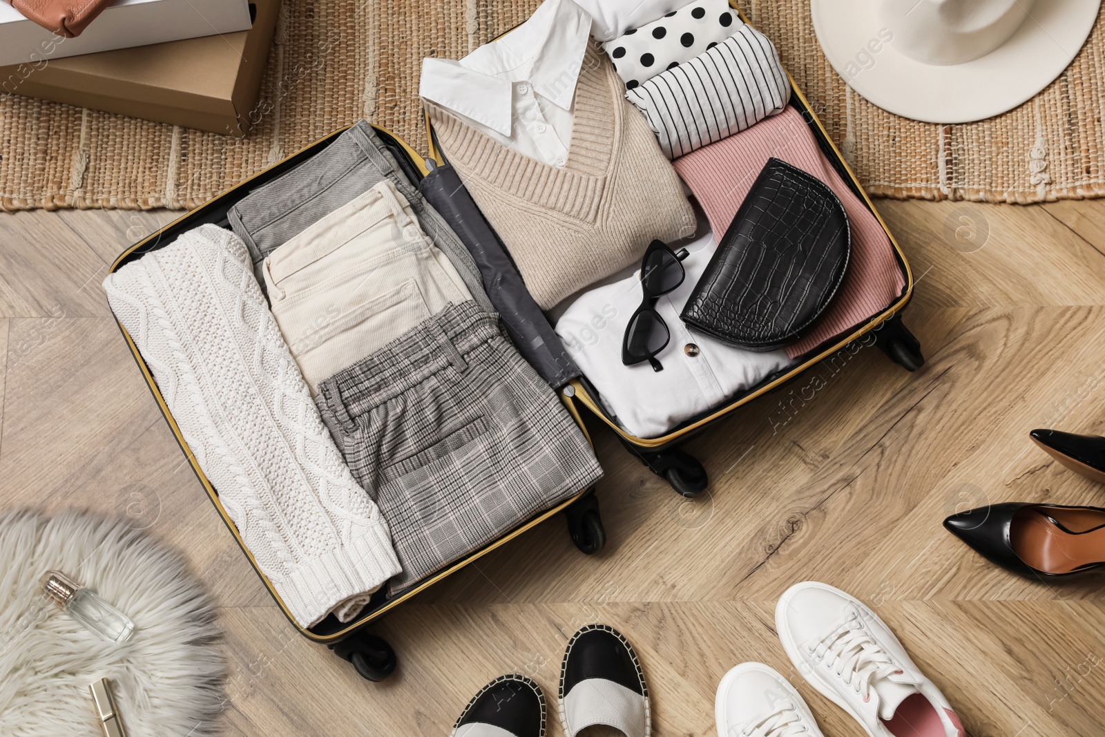 Photo of Open suitcase with folded clothes, accessories and shoes on floor, flat lay