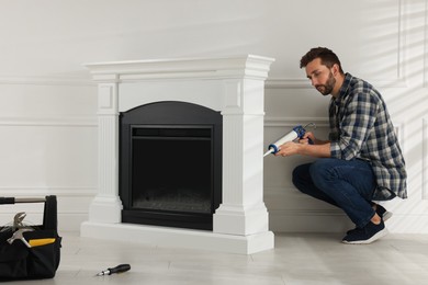 Photo of Man sealing electric fireplace with caulk near white wall in room