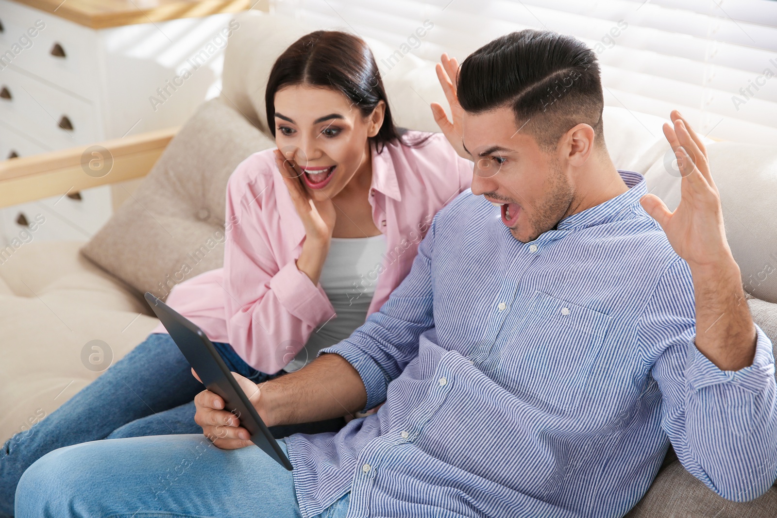 Photo of Emotional couple participating in online auction using tablet at home