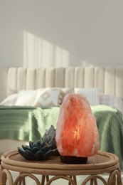 Photo of Beautiful Himalayan salt lamp and lotus figures on wicker table in bedroom, space for text