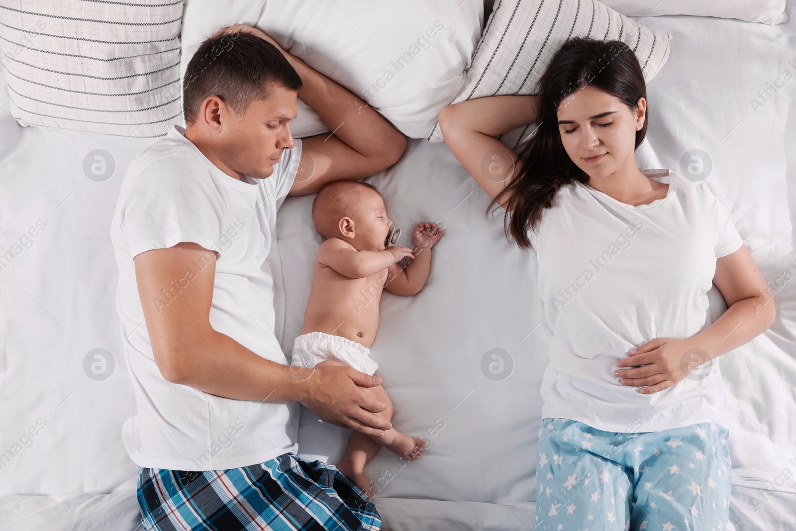 Photo of Couple and baby sleeping on bed together, top view